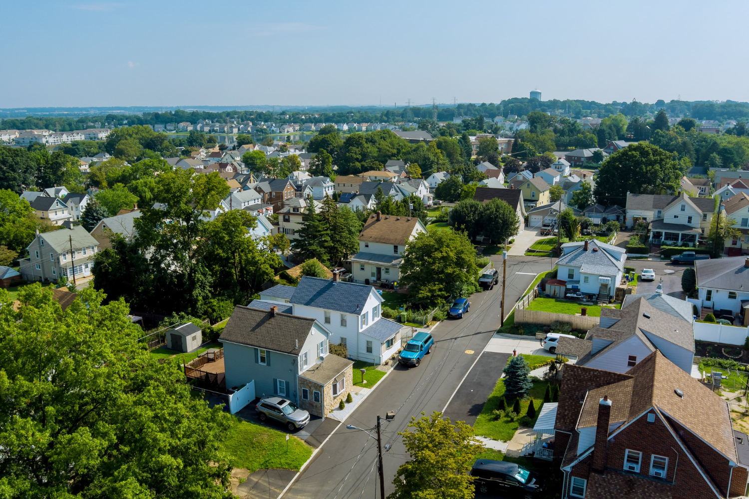 Aerial view of a suburban neighborhood with houses, trees, and parked cars on a sunny day.