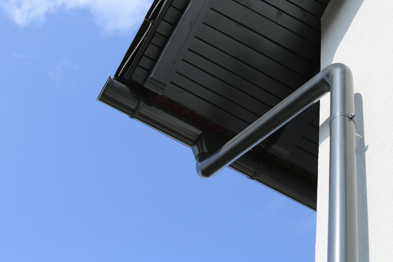 Close-up of roof eaves and a black rain gutter pipe against a clear blue sky.
